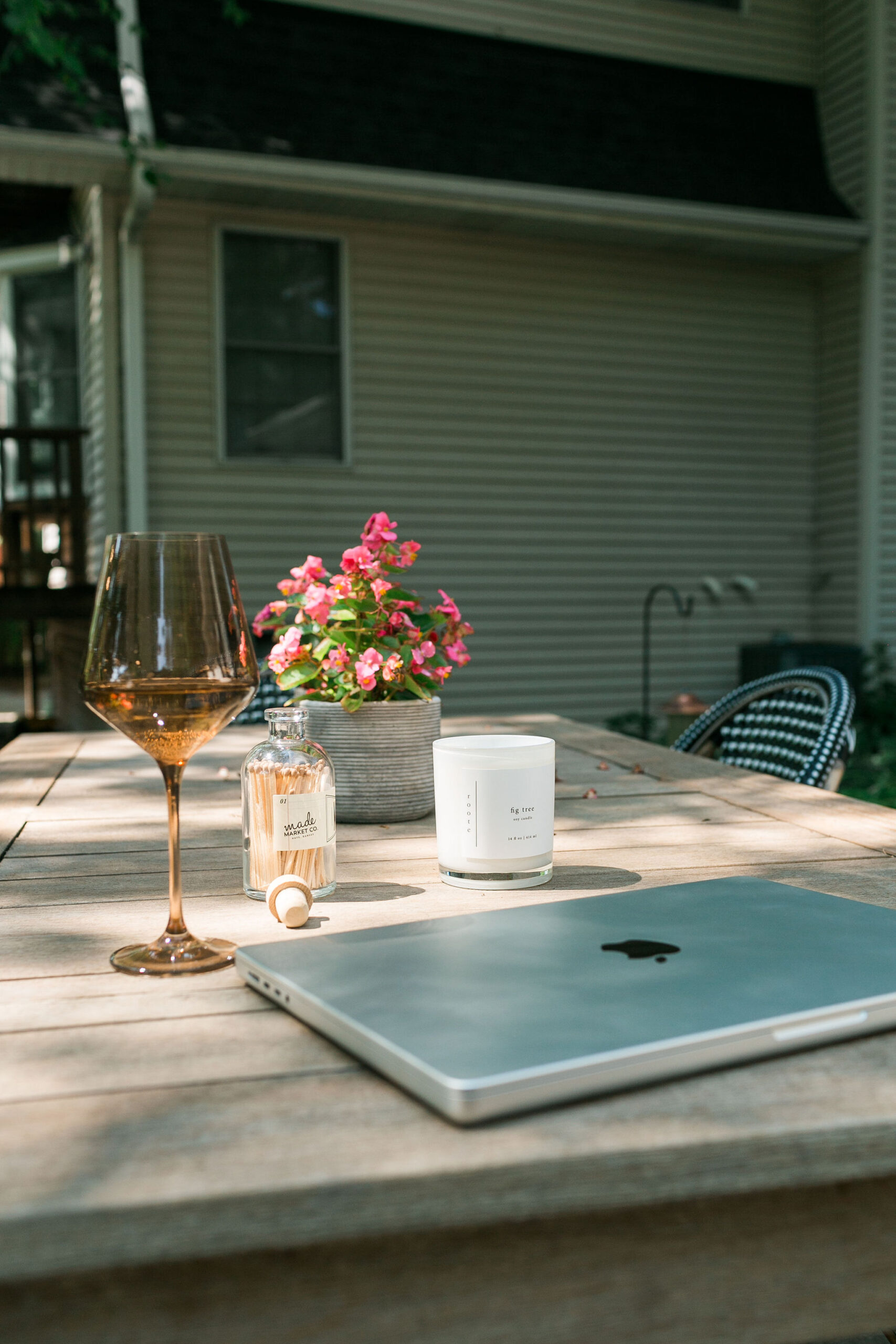 Laptop, glass of wine, and flowers on a backyard deck table, representing a relaxed approach to planning a home move or real estate strategy.
